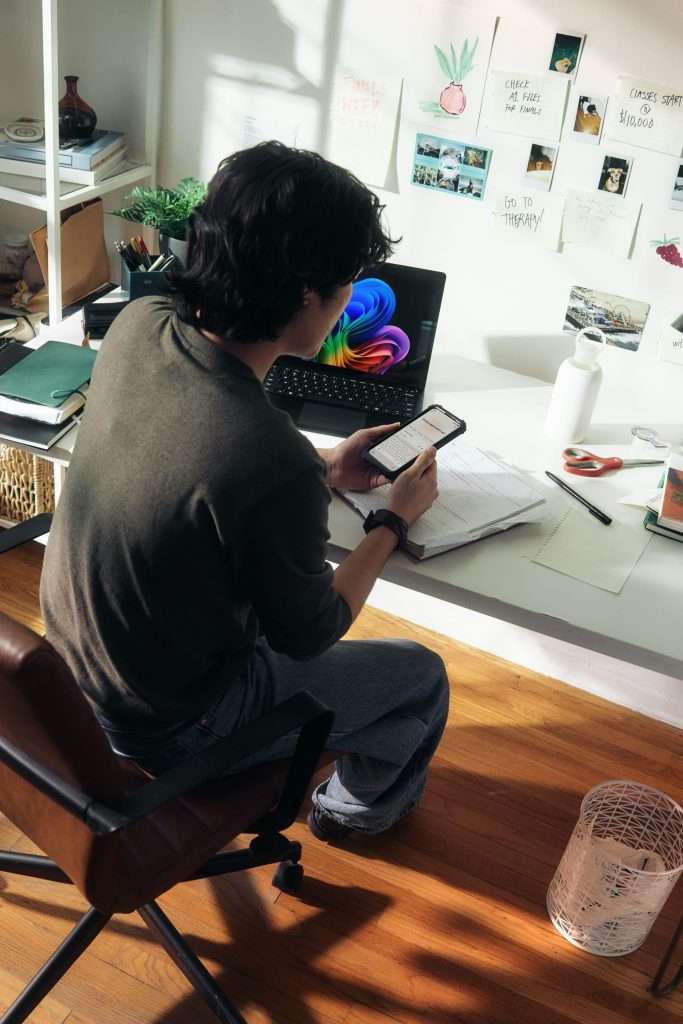 Young remote worker using laptop and smartphone at home office desk to access AI productivity tools